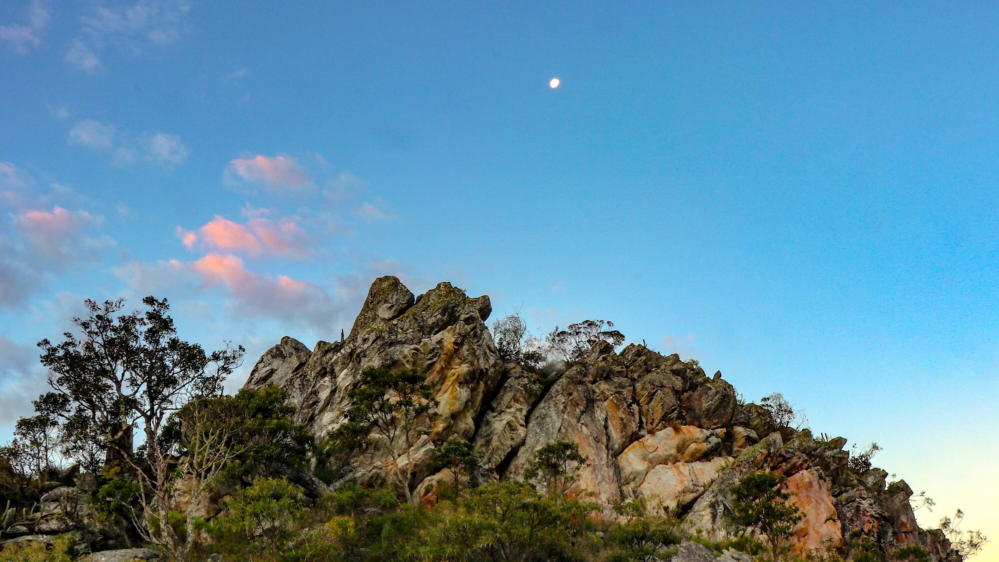 Foto do afloramento rochoso da Lapa da Dança do Sol com a lua ao fundo.